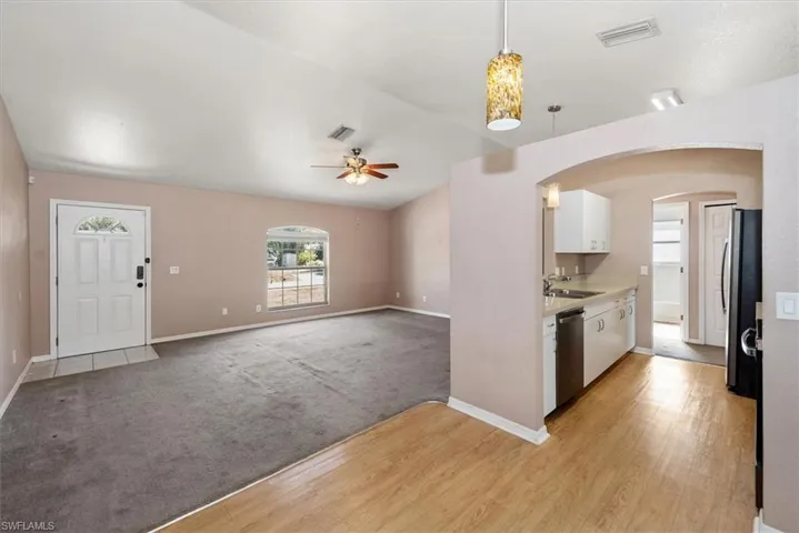 Kitchen featuring light countertops, white cabinetry, open floor plan, arched walkways, and light colored carpet
