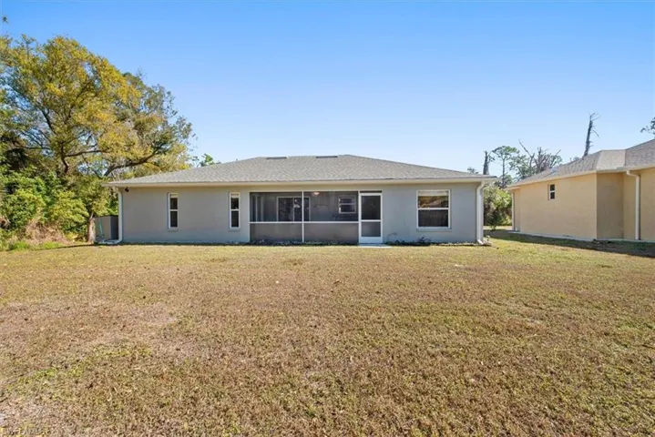 Rear view of house featuring a lawn, a sunroom, and stucco siding