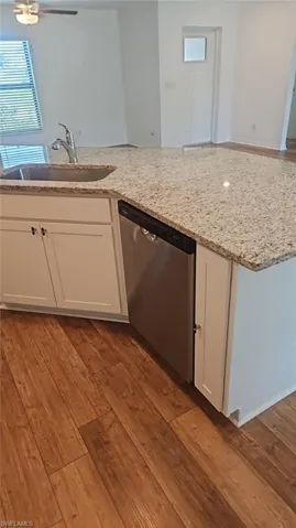 Kitchen island featuring a stainless steel sink with a high-arc faucet, granite countertop, white cabinetry, and a built-in stainless steel dishwasher