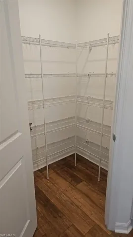 Spacious corner pantry featuring multiple tiers of white wire shelving, wood-finish flooring, and crisp white walls