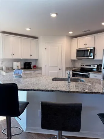 Kitchen featuring white cabinets, light stone countertops, stainless steel appliances, and recessed lighting
