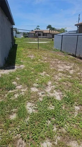 Open parcel featuring partial chain-link fencing, a partially grassed surface, and clear sky overhead
