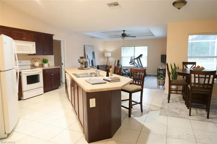 Kitchen with light countertops, white appliances, a breakfast bar area, dark wood finish cabinets, and an island with sink