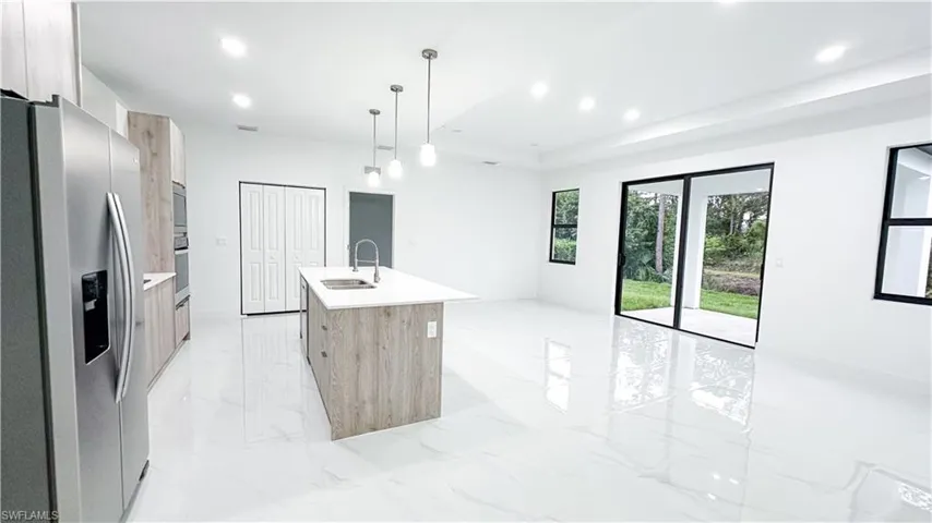 Open-concept living area featuring polished tile flooring, recessed lighting, a modern kitchen island with pendant lighting, and sliding glass doors to outdoor space