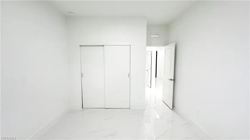 White interior walls, white sliding closet doors, white paneled interior door, and polished tile flooring
