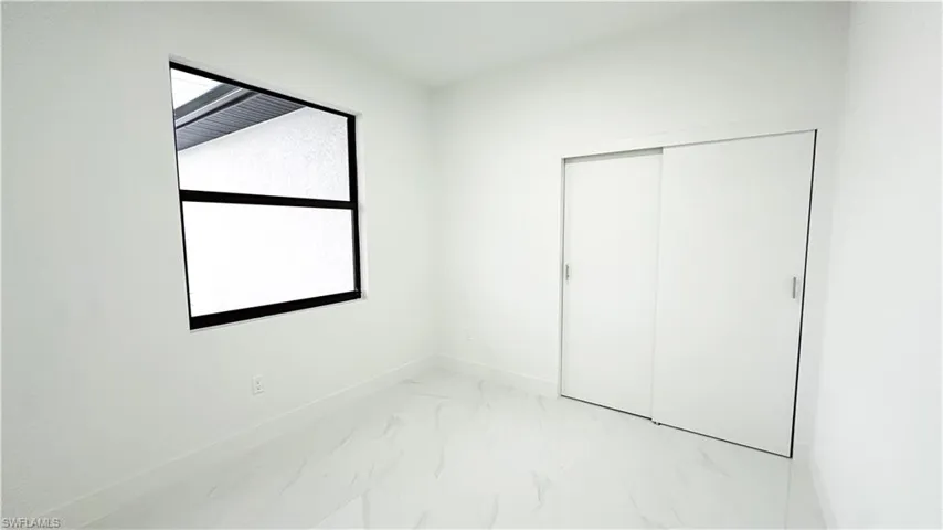 White interior walls, large window with black framing, white sliding closet doors, and light-toned tile flooring