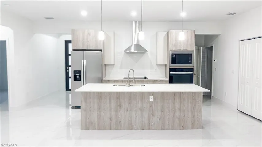 Modern kitchen featuring a central island with an undermount sink, stainless steel appliances, wood-finish cabinetry, and recessed lighting