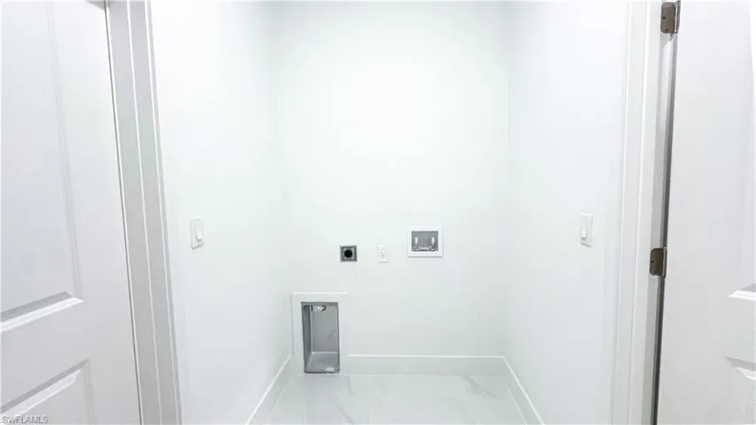 Dedicated utility space featuring white walls, white trim, and a white tiled floor