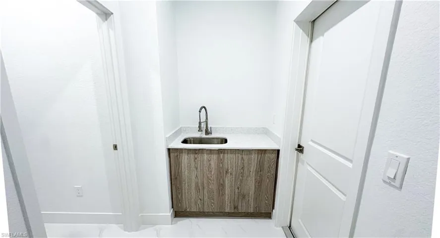 Utility sink with a gooseneck faucet, wood-finish cabinetry, and a light-toned countertop