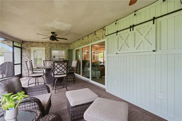 Covered patio featuring wood-finish flooring, stone accent walls, a ceiling fan, and sliding glass doors
