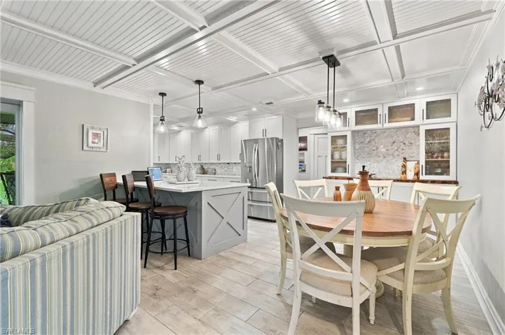 Coffered ceiling with beadboard panels, wood-finish flooring, kitchen island with built-in storage, stainless steel French door refrigerator, and glass-front cabinetry