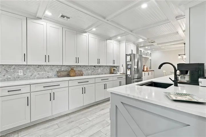 White shaker-style cabinetry with black hardware, complementing a light-toned backsplash and countertops