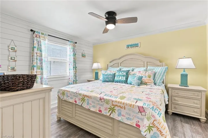 Shiplap accent wall, crown molding, ceiling fan with integrated lighting, wood-finish flooring, and a window with blinds