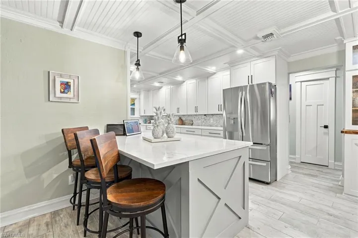Kitchen featuring a large island with a light-toned countertop, white cabinetry with dark hardware, stainless steel refrigerator, and wood-finish flooring