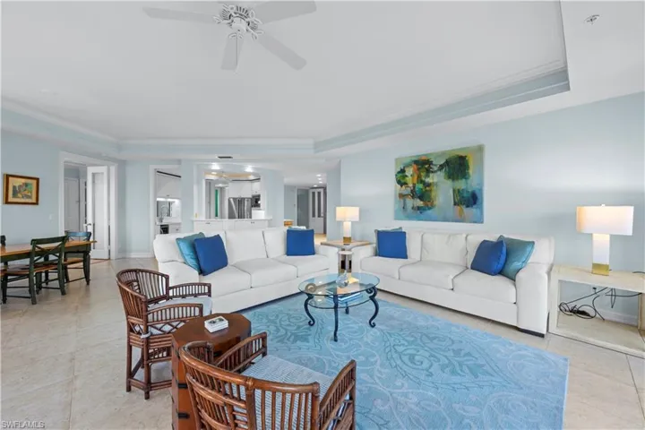 Living room with ceiling fan, a raised ceiling, crown molding, light tile patterned floors, and baseboards