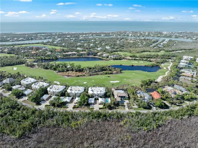 Aerial view of property and surrounding area featuring a golf club, a nearby body of water, and nearby suburban area
