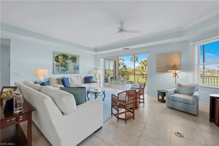 Living area with ornamental molding, a tray ceiling, ceiling fan, baseboards, and light tile patterned floors