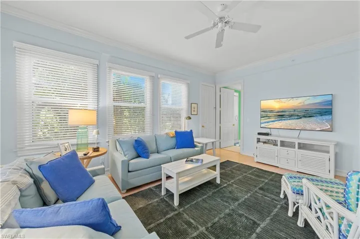 Living room featuring crown molding, ceiling fan, baseboards, and wood finished floors
