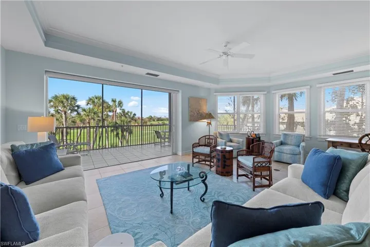 Tiled living room featuring a raised ceiling, ornamental molding, a ceiling fan, and baseboards