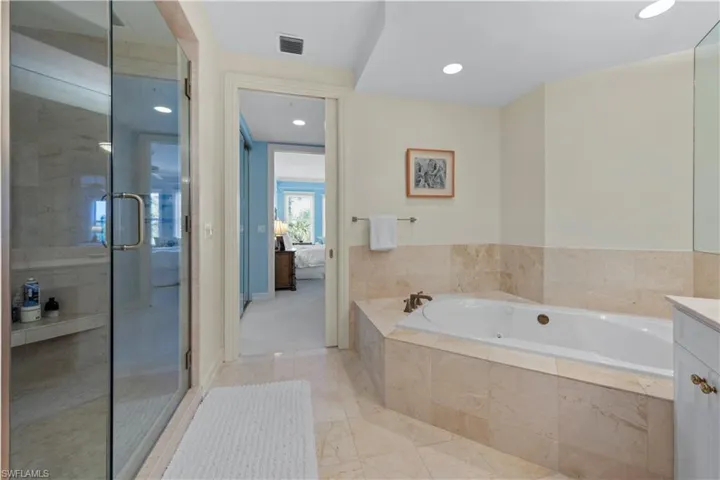 Ensuite bathroom featuring a tub with jets, a stall shower, vanity, recessed lighting, and marble finish floors