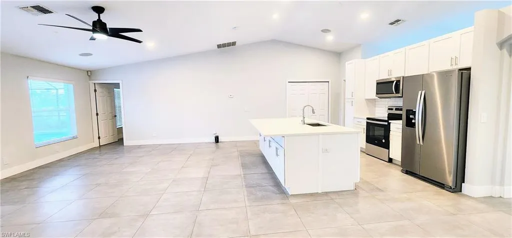 Kitchen featuring lofted ceiling, white cabinets, a center island with sink, sink, and stainless steel appliances