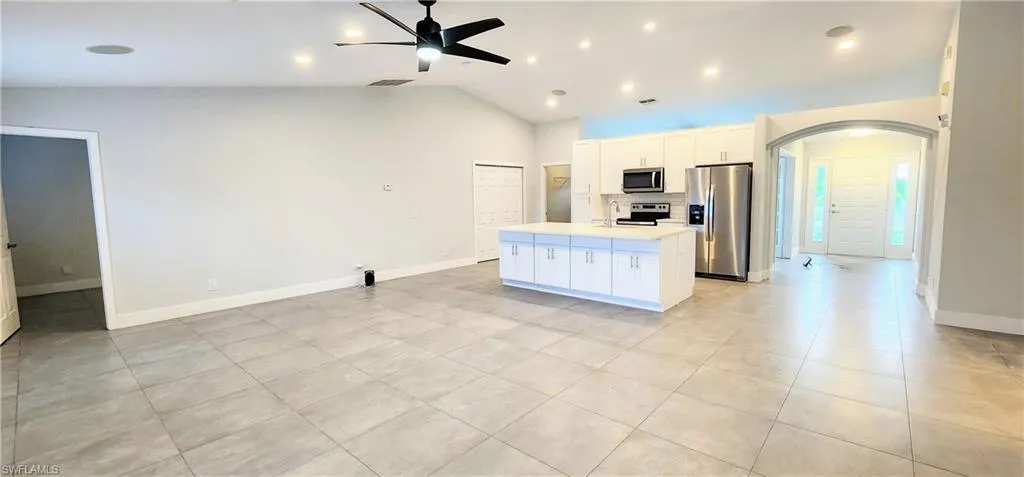 Kitchen featuring a kitchen island, white cabinetry, ceiling fan, stainless steel appliances, and vaulted ceiling