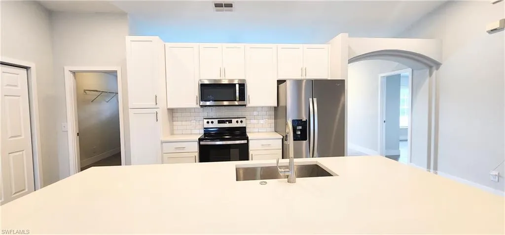 Kitchen with appliances with stainless steel finishes, decorative backsplash, and white cabinets