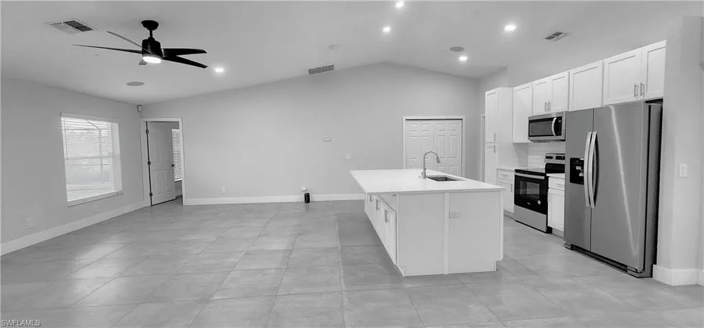 Kitchen featuring appliances with stainless steel finishes, white cabinetry, a kitchen island with sink, vaulted ceiling, and sink