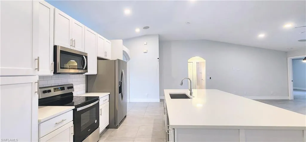 Kitchen with sink, a kitchen island with sink, stainless steel appliances, and white cabinets