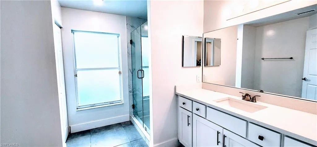 Bathroom featuring a shower with door, vanity, and tile patterned floors