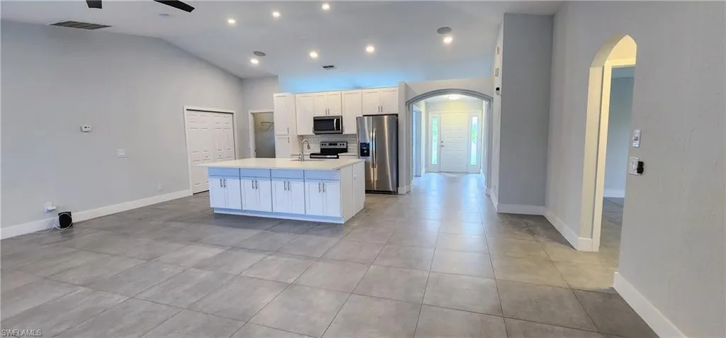 Kitchen with ceiling fan, appliances with stainless steel finishes, an island with sink, white cabinetry, and high vaulted ceiling