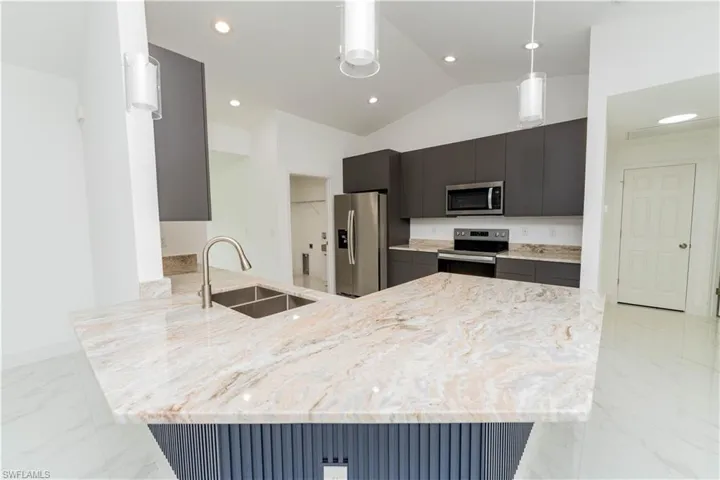 Kitchen featuring a peninsula, light stone countertops, stainless steel appliances, recessed lighting, and hanging light fixtures