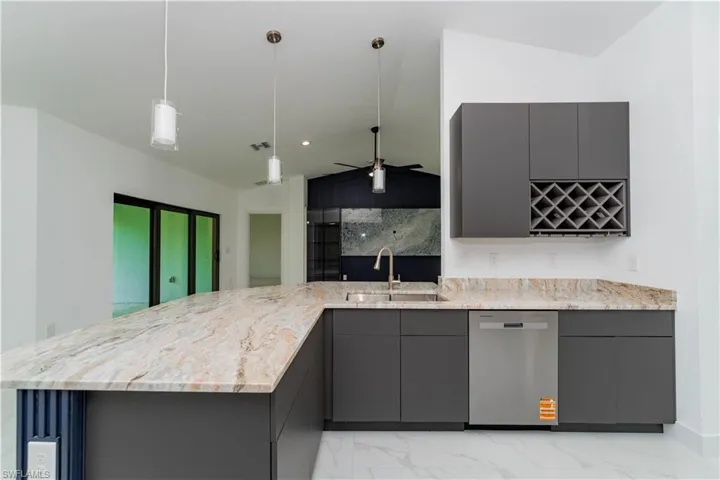 Kitchen featuring modern cabinets, gray cabinets, light marble finish flooring, vaulted ceiling, and light stone counters