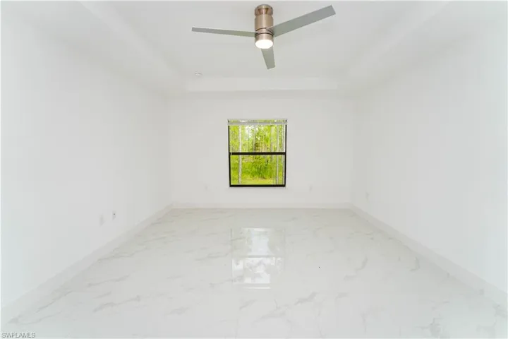 Empty room featuring a raised ceiling, light marble finish floors, and a ceiling fan