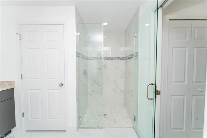 Bathroom with a closet, a marble finish shower, vanity, and recessed lighting