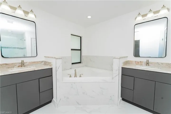 Bathroom featuring a bath, two vanities, a marble finish shower, recessed lighting, and light marble finish floors