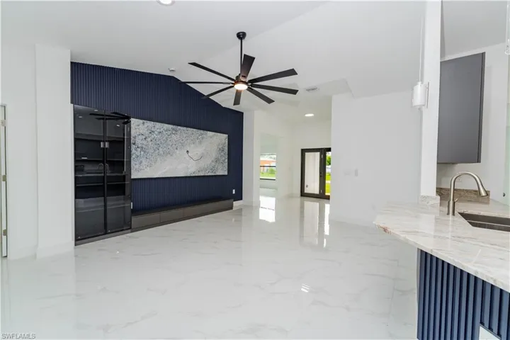 Unfurnished living room featuring light marble finish floors, vaulted ceiling, an accent wall, recessed lighting, and a ceiling fan