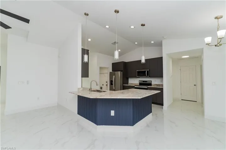 Kitchen with dark cabinets, light stone counters, a peninsula, stainless steel appliances, and decorative light fixtures