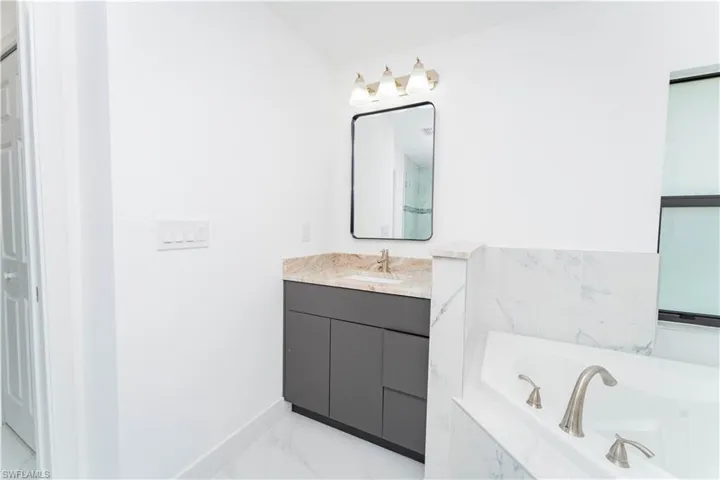Bathroom featuring vanity, a garden tub, and light marble finish flooring
