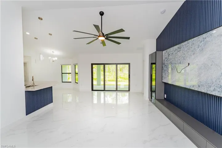 Unfurnished living room with light marble finish flooring, vaulted ceiling, a chandelier, and ceiling fan
