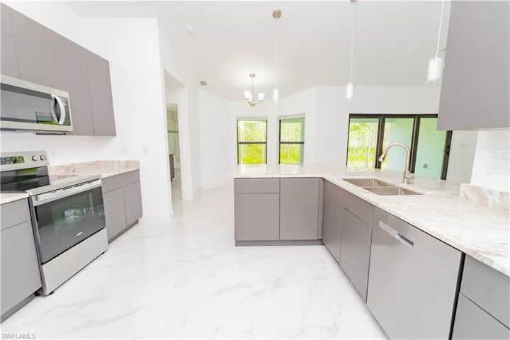 Kitchen featuring gray cabinetry, appliances with stainless steel finishes, pendant lighting, and light marble finish flooring