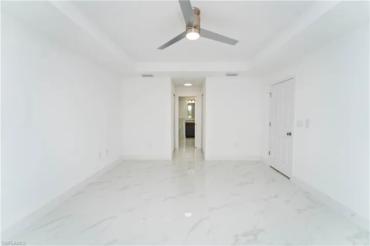 Spare room featuring a raised ceiling, light marble finish floors, and a ceiling fan