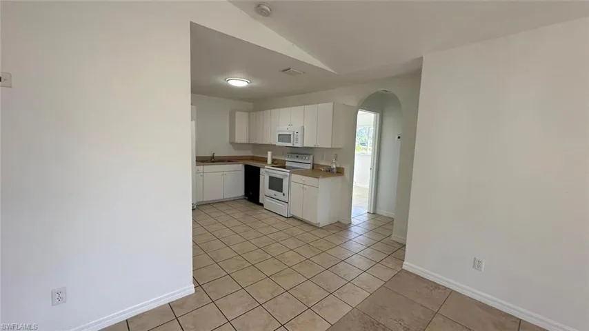 Kitchen featuring arched walkways, white appliances, white cabinetry, light tile patterned flooring, and vaulted ceiling