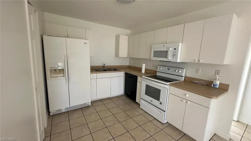 Kitchen featuring white appliances, white cabinets, light tile patterned floors, and light countertops