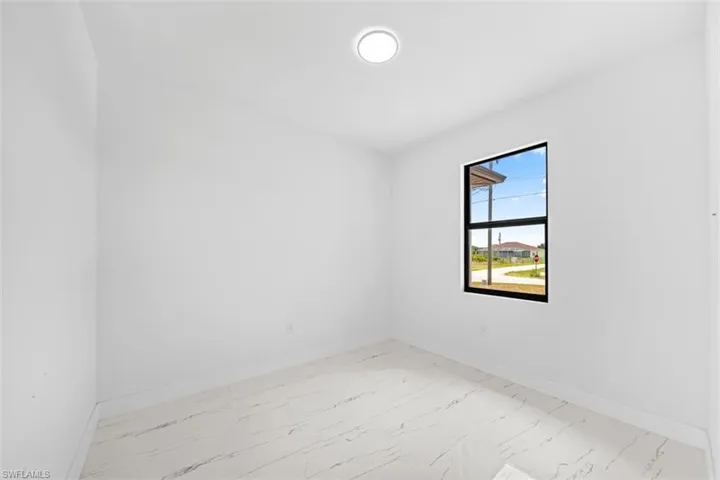 White interior walls with a single window, a flush mount ceiling light, and marble-look tile flooring
