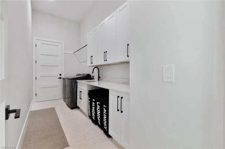 Clothes washing area featuring sink, washer / dryer, and cabinets