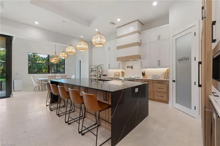 Kitchen with sink, white cabinets, a large island with sink, hanging light fixtures, and a raised ceiling