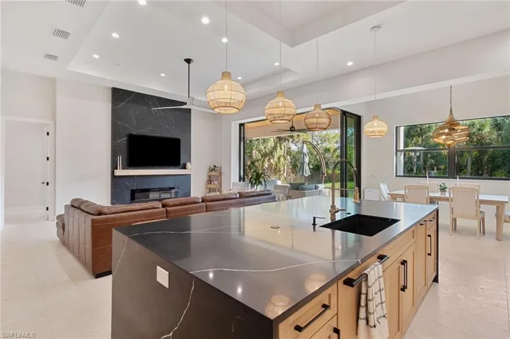 Kitchen with sink, a large island with sink, light brown cabinets, a raised ceiling, and a premium fireplace