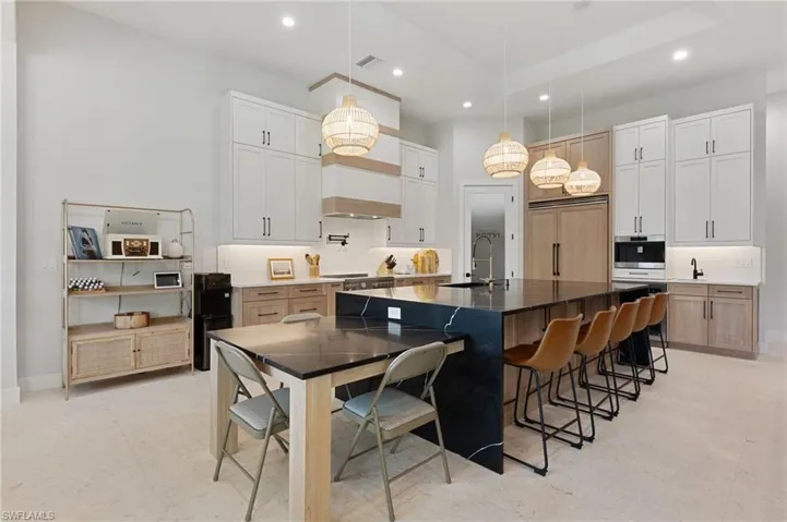 Kitchen featuring sink, hanging light fixtures, a spacious island, white cabinets, and a kitchen bar