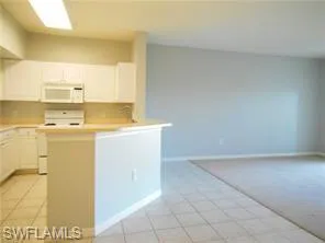 Kitchen with white cabinetry, light countertops, white appliances, light tile patterned flooring, and a peninsula